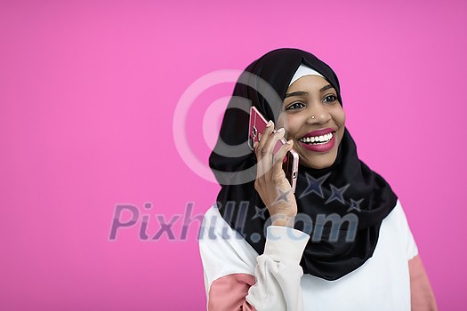 a beautiful afro girl smiling broadly uses a cell phone in front of a pink background
