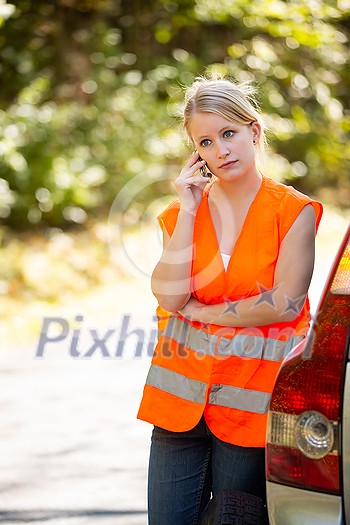 Young female driver wearing a high visibility vest, calling the roadside service/assistance after her car has broken down