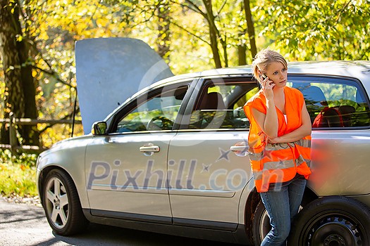 Young female driver wearing a high visibility vest, calling the roadside service/assistance after her car has broken down