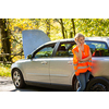 Young female driver wearing a high visibility vest, calling the roadside service/assistance after her car has broken down