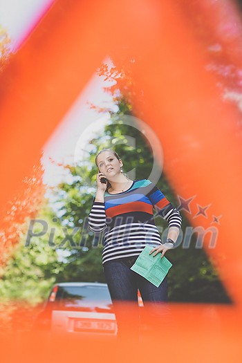 Pretty, young woman with her car broken down by the roadside, setting up the safety triangle, waiting for assistance