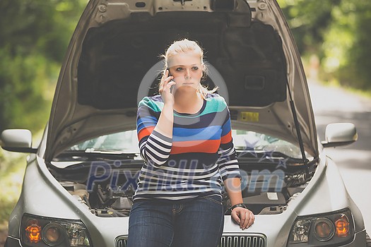 Pretty, young woman with her car broken down by the roadside, setting up the safety triangle, waiting for assistance