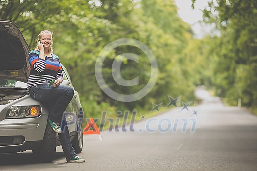 Pretty, young woman with her car broken down by the roadside, setting up the safety triangle, waiting for assistance