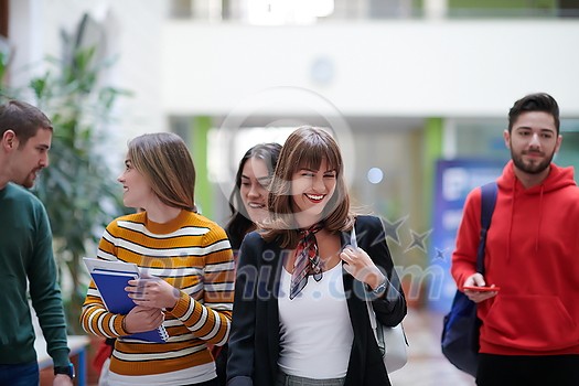 a group of students with books, a laptop and smartphones talk in a modern college