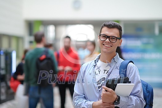 a student in glasses stands in the hallway of a modern college and uses a laptop