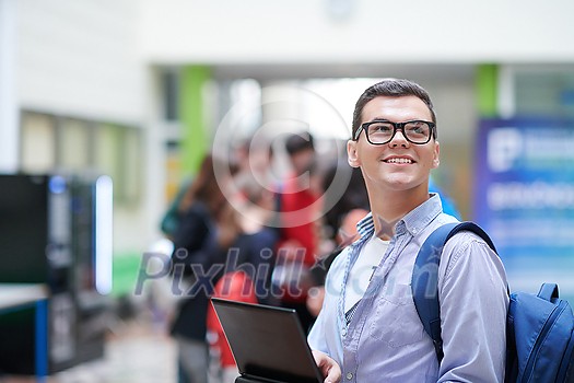 a student in glasses stands in the hallway of a modern college and uses a laptop