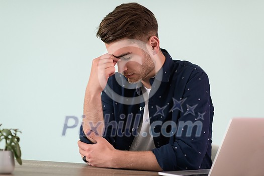 a disappointed and annoyed man sitting at a table and looking at a laptop
