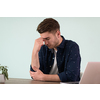 a disappointed and annoyed man sitting at a table and looking at a laptop
