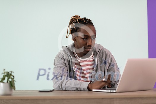 an afro young man sits in his home office during a pandemic and uses laptop for online meeting 
