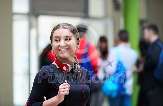 portrait of a happy young student getting ready for class while waiting in the college hallway with headphones and laptop