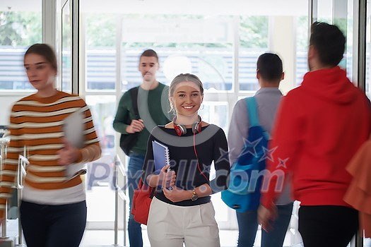 portrait of a happy young student getting ready for class while waiting in the college hallway with headphones and notes