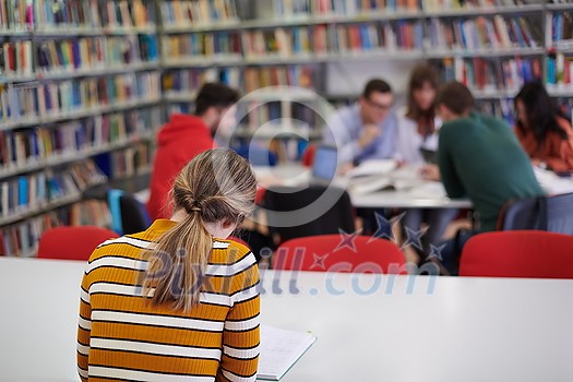 Female student taking notes from a book at library. Young woman sitting at table doing assignments in college library. Female student taking notes from a book at library. Young woman sitting at table doing assignments in college library.