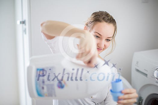 Housework: young woman doing laundry - putting colorful garments into the washing machine (shallow DOF; color toned image)