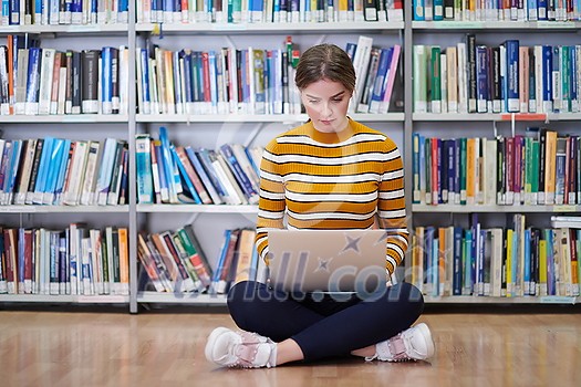 Woman student taking notes from a book at library. Young woman sitting and doing assignments in college library.