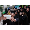education, graduation, technology and people concept - group of happy international students in mortar boards and bachelor gowns with diplomas taking selfie by smartphone