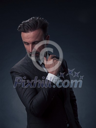 Portrait of a successful stylish elegant senior businessman with a grey beard and casual business clothes confident in photo studio isolated on dark background gesturing with hands. High-quality photo