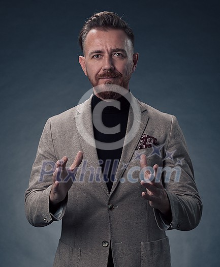 Portrait of a successful stylish elegant senior businessman with a grey beard and casual business clothes confident in photo studio isolated on dark background gesturing with hands. High-quality photo