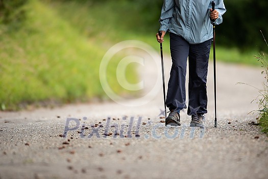 Senior person staying fit by doing daily cardio exercise, going for a fast paced power walk with sticks Senior person staying fit by doing daily cardio exercise, going for a fast paced power walk with sticks