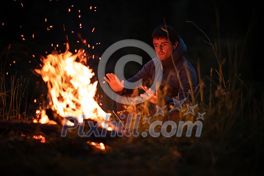 Young man making fire while camping outdoors, in an alpine wilderness - warming up his hands