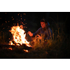 Young man making fire while camping outdoors, in an alpine wilderness - warming up his hands