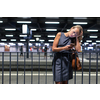 Exhausted overworked young female commuter waiting for her daily train in a modern trainstation, using her cellphone while waiting (color toned image)