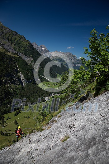 Pretty, female climber on a via ferrata - climbing on a rock in Swiss Alps