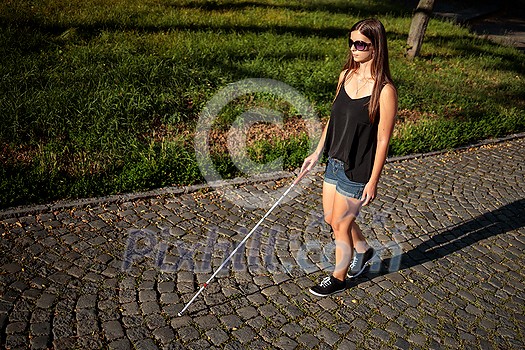 Blind woman walking on city streets, using her white cane to navigate the urban space better and to get to her destination safely Blind woman walking on city streets, using her white cane to navigate the urban space better and to get to her destination safely