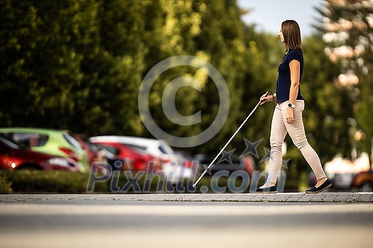 Blind woman walking on city streets, using her white cane to navigate the urban space better and to get to her destination safely Blind woman walking on city streets, using her white cane to navigate the urban space better and to get to her destination safely