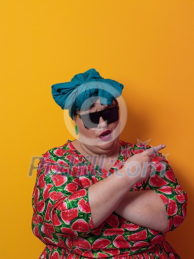 Funny plus size sexy model woman with trendy sunglasses, fashionable overweight blonde in colorful dress posing at the yellow fortuna gold background in studio. High quality photo Funny plus size sexy model woman with trendy sunglasses, fashionable overweight blonde in colorful dress posing at the yellow fortuna gold background in studio. High quality photo