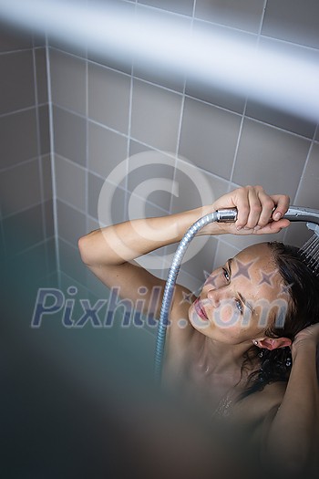 Pretty, young woman taking a long hot shower washing her hair in a modern design bathroom