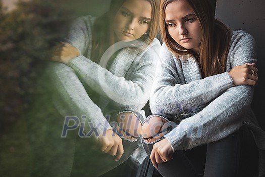 Depressed and anxious young woman sitting by a large window, feeling blue, sad, uncertain Depressed and anxious young woman sitting by a large window, feeling blue, sad, uncertain