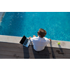 A modern elderly man enjoys the pool while working on his laptop next to a modern luxury house. Selective focus. High-quality photo
