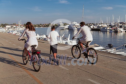 Happy family enjoying a beautiful morning by the sea together, parents riding a bike and their son riding an electric scooter. Selective focus. High-quality photo