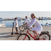 Happy family enjoying a beautiful morning by the sea together, parents riding a bike and their son riding an electric scooter. Selective focus. High-quality photo