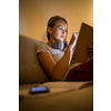 Pretty, young woman working at home in the evening - using her tablet computer as well as bluetooth headphones, writing down some ideas for tomorrow