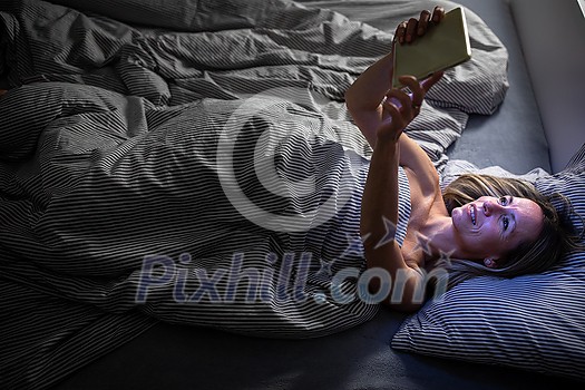 Middle-aged woman using her tablet computer before sleep in bed in the evening - exposure to blue light right before sleep Middle-aged woman using her tablet computer before sleep in bed in the evening - exposure to blue light right before sleep
