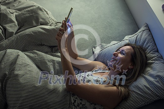 Pretty, middle-aged woman using her tablet computer before sleep in bed in the evening