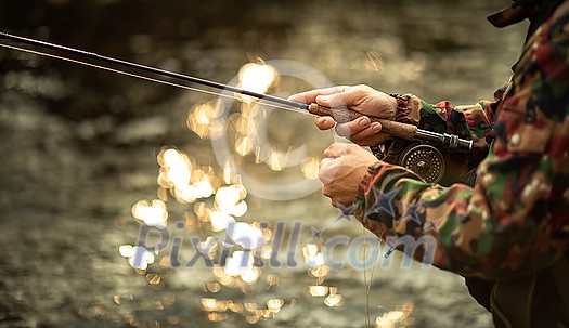 Close-up view of the hands of a fly fisherman working the line and the fishing rod while fly fishing on a splendid mountain river for rainbow trout Close-up view of the hands of a fly fisherman working the line and the fishing rod while fly fishing on a splendid mountain river for rainbow trout