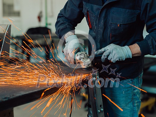 Heavy Industry Engineering Factory Interior with Industrial Worker Using Angle Grinder and Cutting a Metal Tube. Contractor in Safety Uniform and Hard Hat Manufacturing Metal Structures. High-quality photo Heavy Industry Engineering Factory Interior with Industrial Worker Using Angle Grinder and Cutting a Metal Tube. Contractor in Safety Uniform and Hard Hat Manufacturing Metal Structures. High-quality photo