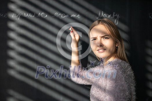 Pretty, young female student in front of a blackboard during class Pretty, young female student in front of a blackboard during class