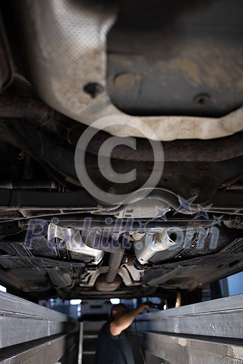 Car mechanic under a car in a repair shop/car garage (shallow DOF/color toned image) Car mechanic under a car in a repair shop/car garage (shallow DOF/color toned image)