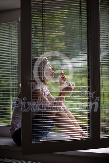 Mid-aged woman lighting a cigarette at home, getting her nicotine daily dose, unable to resist to her unhealthy habit Mid-aged woman lighting a cigarette at home, getting her nicotine daily dose, unable to resist to her unhealthy habit
