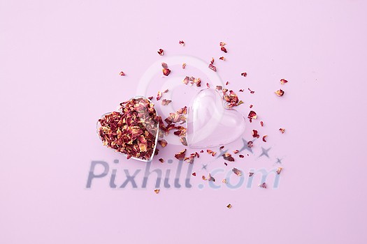 Little transparent heart-shaped pendant full of dried red rose petals on toned background with copy space. Minimal wedding invitation card design.
