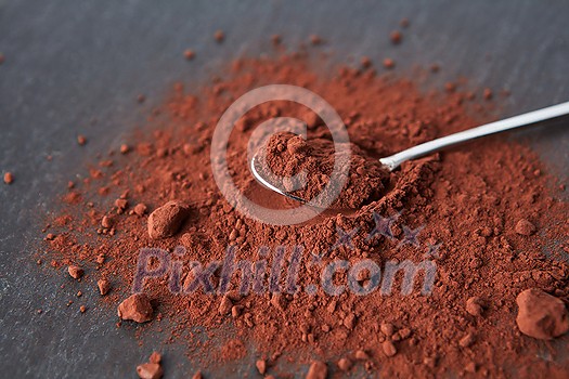 From above of teaspoon placed on heap of bitter cocoa powder of dark brown color on gray background From above of teaspoon placed on heap of bitter cocoa powder of dark brown color on gray background