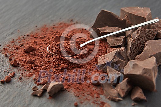 Arranged shiny teaspoon on pile of dry cocoa powder and heap of organic chocolate pieces on gray surface Arranged shiny teaspoon on pile of dry cocoa powder and heap of organic chocolate pieces on gray surface