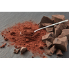 Arranged shiny teaspoon on pile of dry cocoa powder and heap of organic chocolate pieces on gray surface