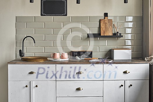 Elegant kitchen with old fashion copper sink and modern faucet, grayish tiles wall, cabinets, tea and coffee containers, pink cups, and magazin on wooden counter. Country house kitchen concept. Elegant kitchen with old fashion copper sink and modern faucet, grayish tiles wall, cabinets, tea and coffee containers, pink cups, and magazin on wooden counter. Country house kitchen concept.