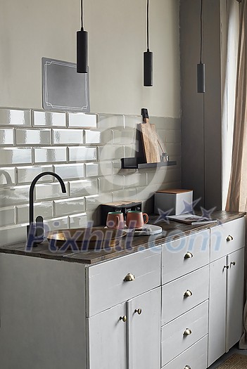 Modern creative idea of small kitchen with gray tiles wall with old fashion copper sink and modern faucet, tea and coffee containers, pink cups, and magazine on wooden counter.