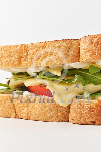 Closeup of delicious melted yellow cheese and arugula leaves between crunchy white bread toasted slices with golden crust placed on white background