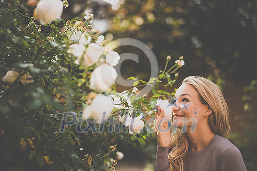 Lifestyle portrait of a young, pretty woman smelling some lovely roses in a garden